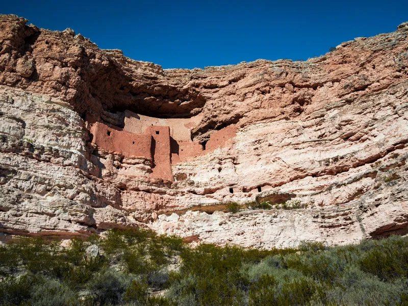 Montezuma Castle ancient cliff dwelling set into a red rock cliff under a deep blue Arizona sky