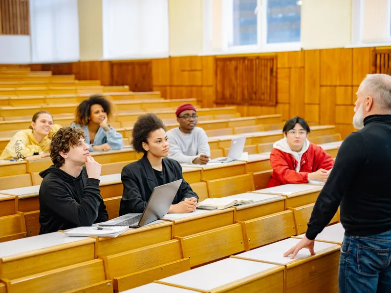 Professor addressing undergraduate students seated at wooden tiered desks in a university lecture hall