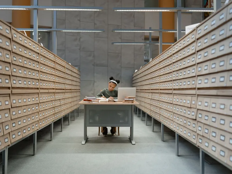 Researcher working at a desk between long rows of library card catalog drawers