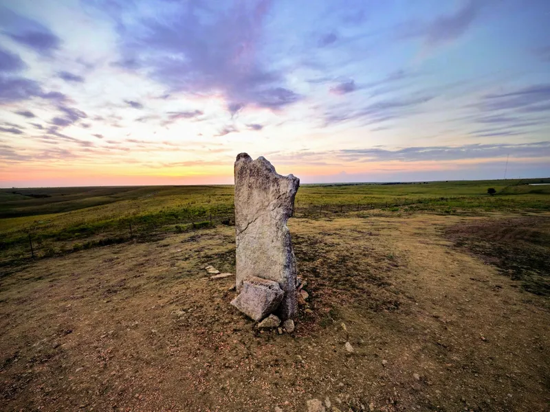 Lone limestone post standing on open Kansas prairie at sunset under a colorful sky