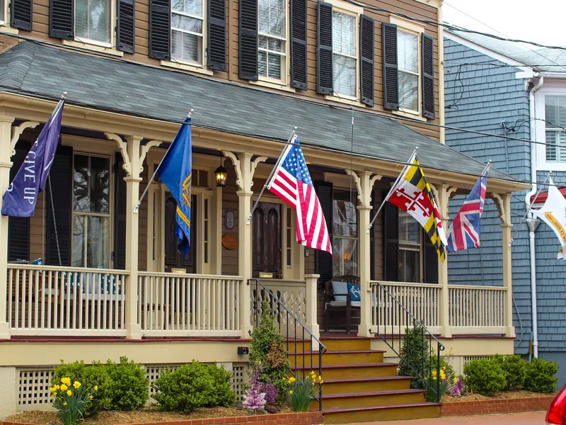 Historic Annapolis house with a wraparound porch decorated with flags including the Maryland flag