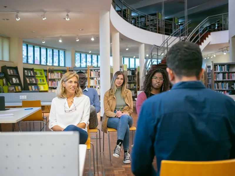 Graduate students and a teacher listen to a classmate's presentation in a library seminar