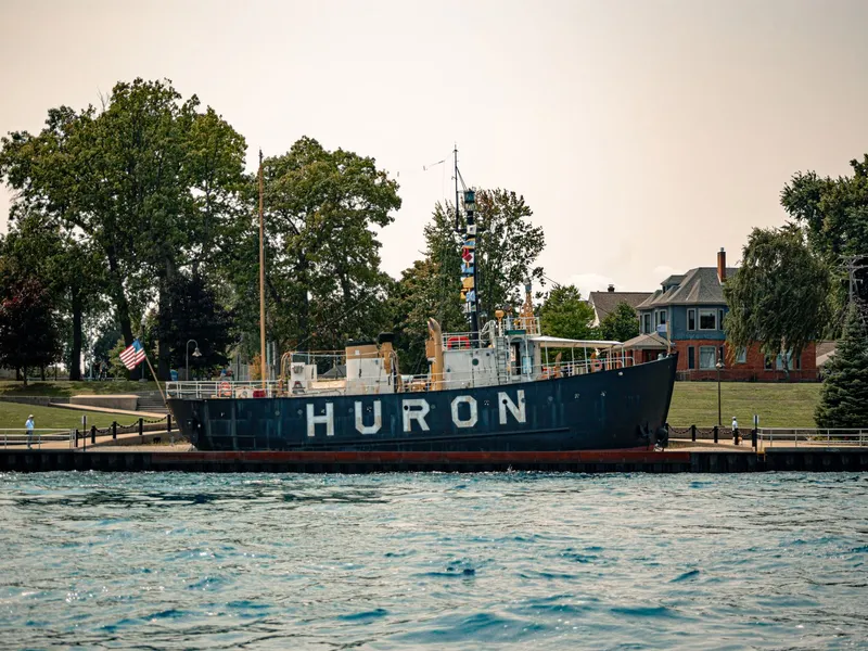 Historic Huron lightship docked along the waterfront with trees and houses behind it