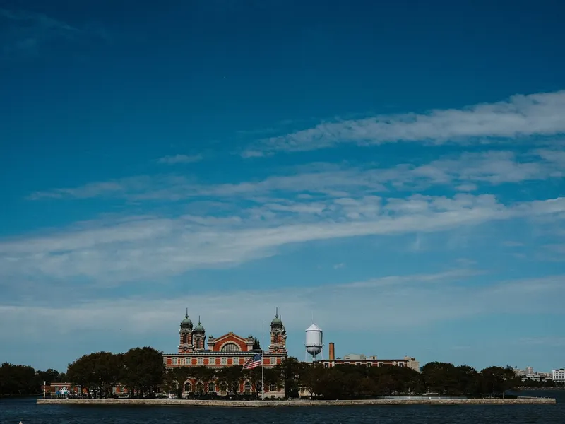 Ellis Island Immigration Museum building across the water beneath a wide blue sky
