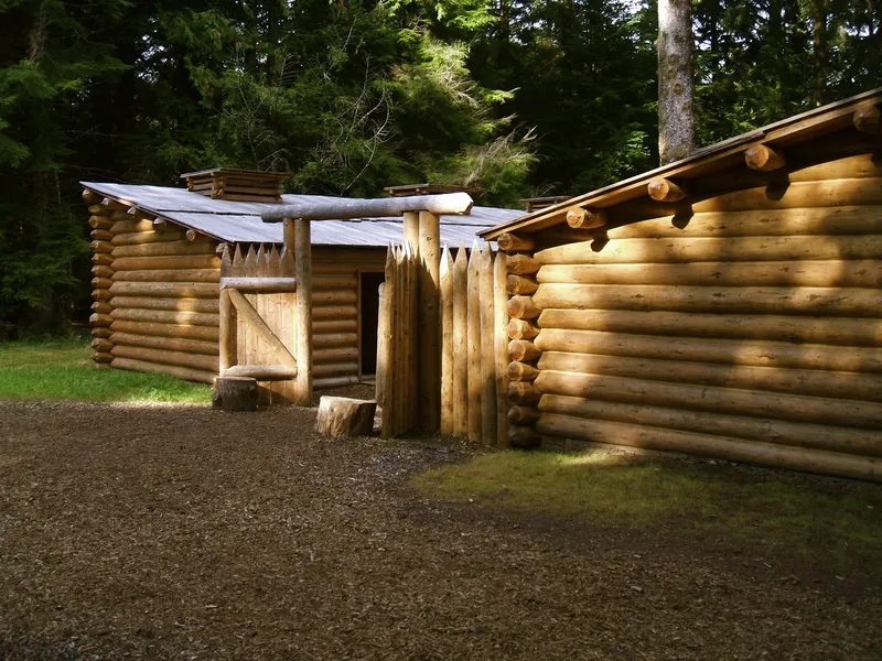 Log cabin buildings and pointed stockade gate of the Fort Clatsop replica among evergreen trees in Oregon