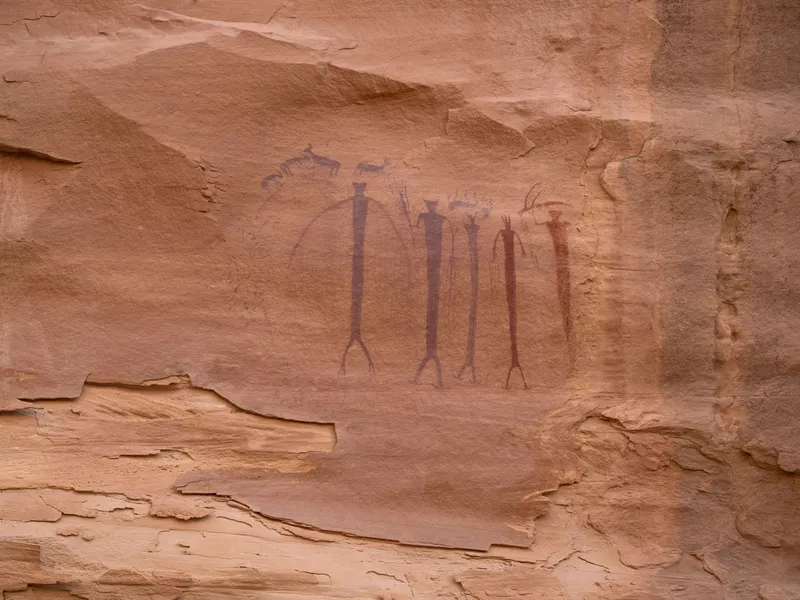 Ancient pictographs of tall human and animal figures painted on a sandstone cliff face in Utah