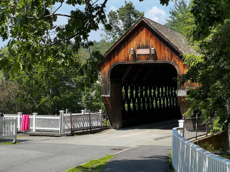 Historic wooden covered bridge framed by summer trees and a white picket fence in Vermont