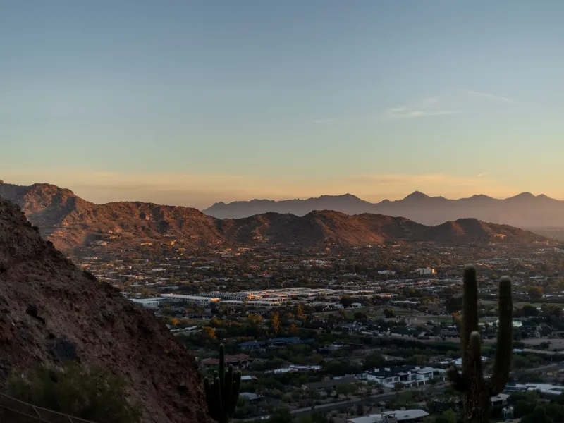 Phoenix, Arizona cityscape beneath desert mountains at sunset with saguaro cacti in the foreground