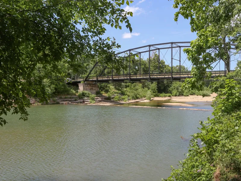 Iron truss War Eagle Bridge crossing a quiet river framed by green trees in northwest Arkansas