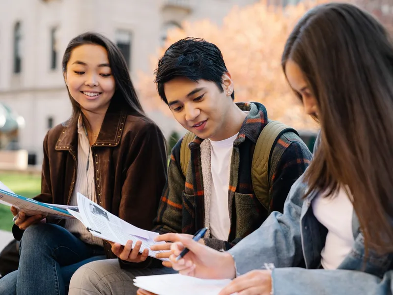 Three community college students sharing papers and notes on campus in autumn