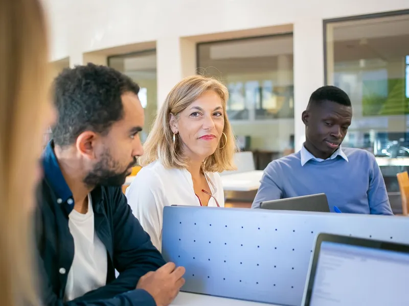Graduate students and a teacher working on research at laptops around a shared table