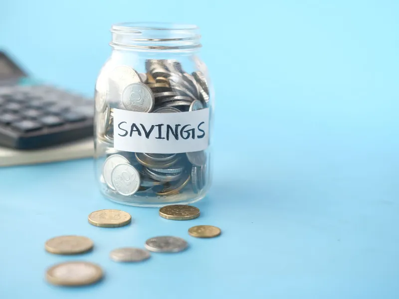 Glass savings jar of coins beside a calculator on a light blue surface