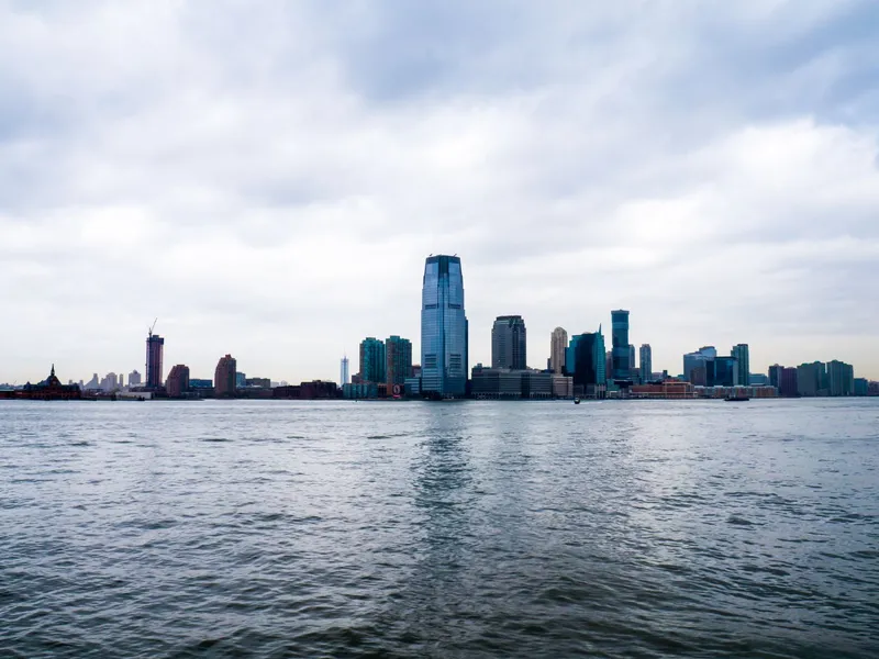 Jersey City skyscrapers beside the Hudson River under a cloudy sky
