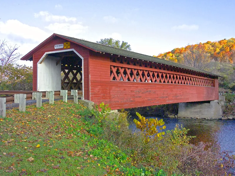 Red covered bridge over a river in Vermont surrounded by autumn color