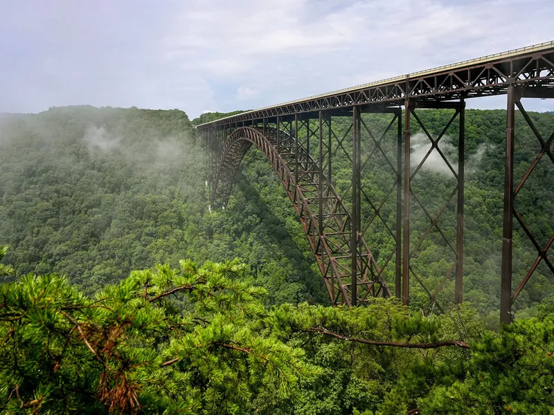 New River Gorge Bridge steel arch above misty green forest in West Virginia