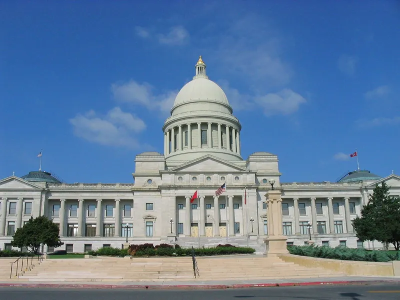 Arkansas State Capitol in Little Rock with its white dome, columns and flags beneath a bright blue sky