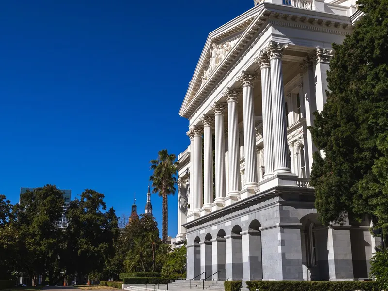White-columned classical facade of the California State Capitol in Sacramento beneath a deep blue sky