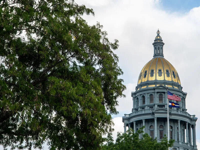 Gold dome of the Colorado State Capitol in Denver with American and Colorado flags beside a tree