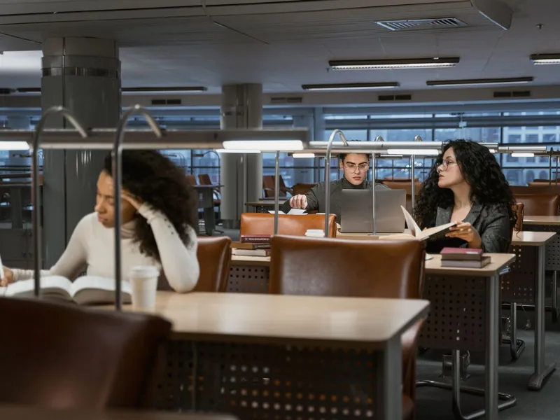 College students researching with books and laptops at tables in a quiet library