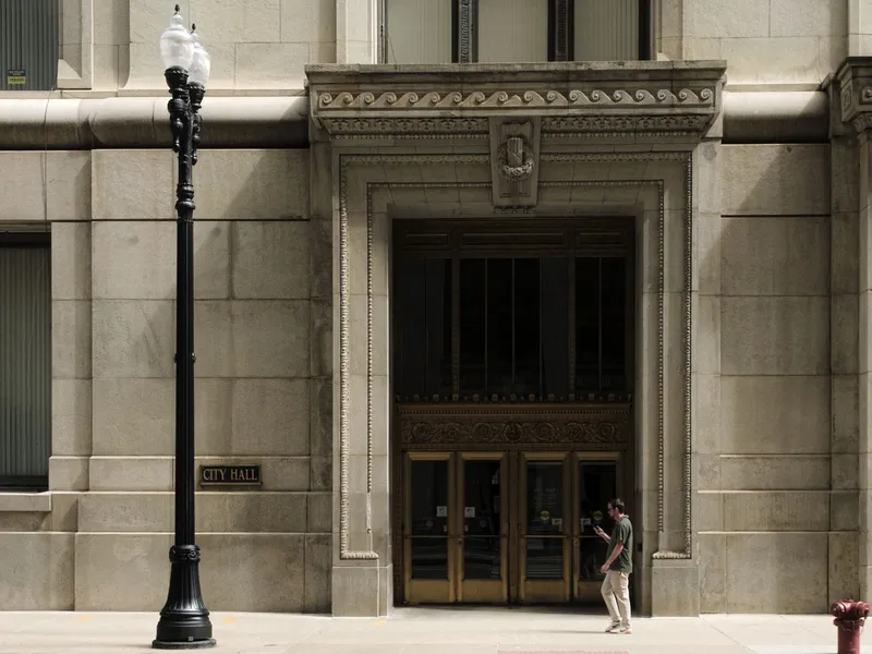 Stone entrance of Chicago City Hall with ornate carved details, a street lamp and a passing pedestrian