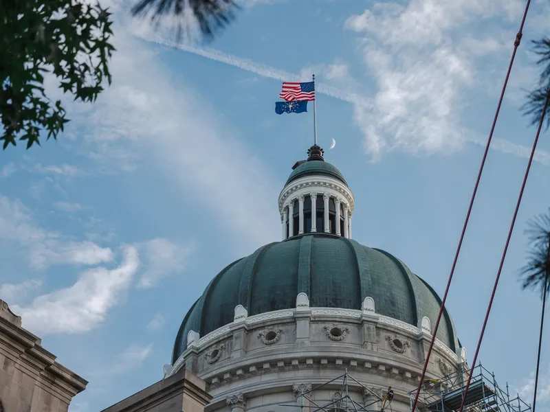 Indiana State Capitol dome with American and Indiana flags against a blue sky