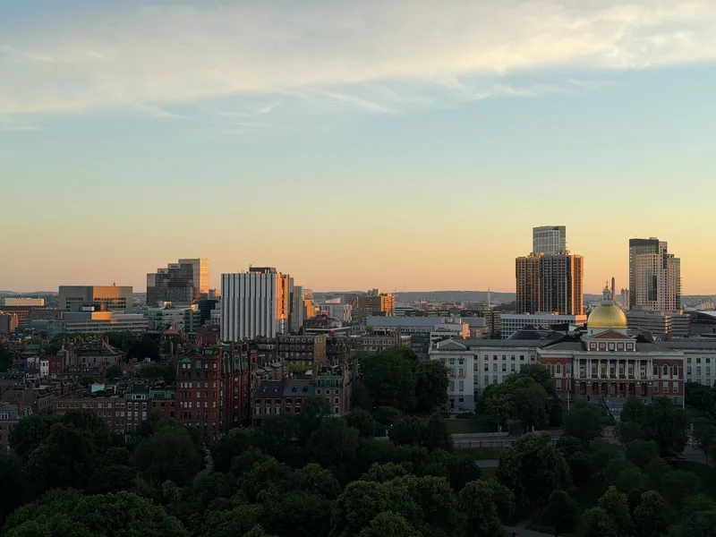 Boston skyline at sunset with the gold dome of the Massachusetts State House among brick buildings and trees