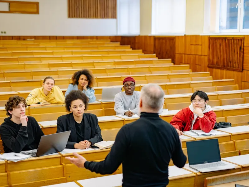 Professor leading a discussion with students and open laptops in a university lecture hall