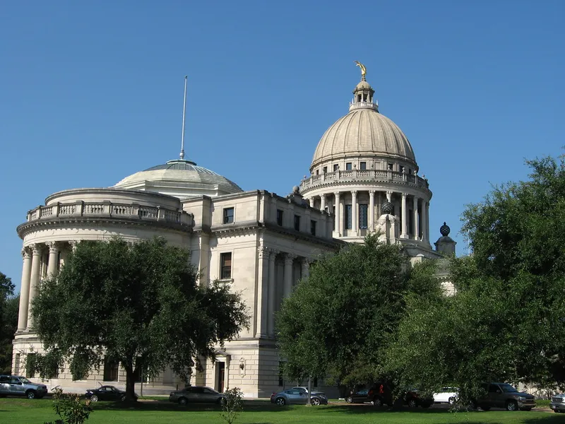 Mississippi State Capitol in Jackson with its stone dome and rotunda behind green oak trees