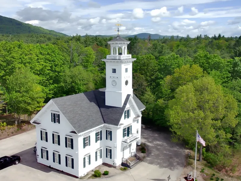 Historic white town hall with a clock tower and cupola surrounded by green trees in Effingham, New Hampshire
