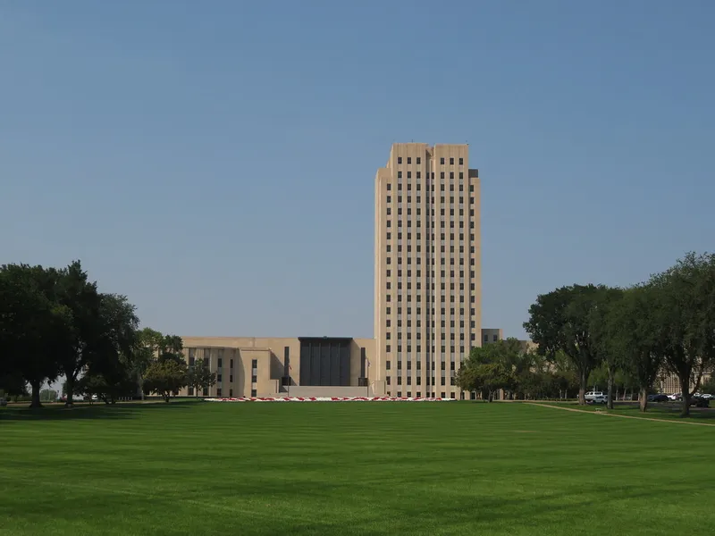 North Dakota State Capitol tower rising behind a wide green lawn and trees in Bismarck