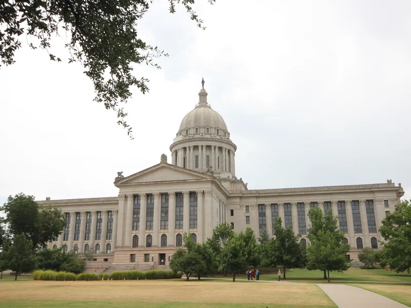 Oklahoma State Capitol with its domed rotunda and columned facade, framed by trees and lawn
