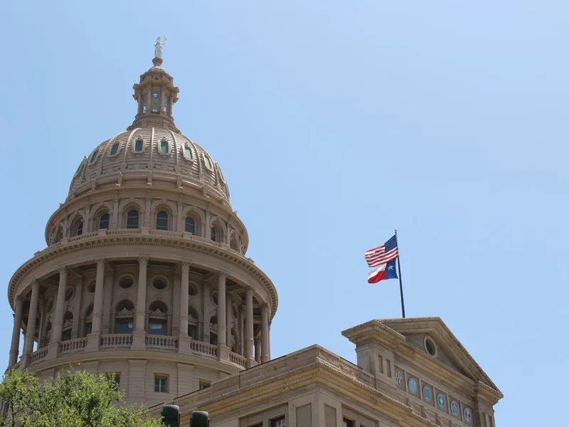 Texas State Capitol dome with American and Texas flags against a clear sky in Austin