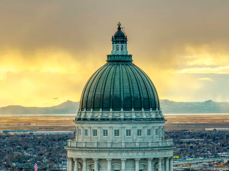 Copper-green dome of the Utah State Capitol against a golden sunset sky above Salt Lake City