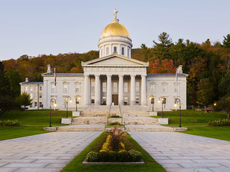 Vermont State House in Montpelier with its gold dome and granite columns before autumn hillside