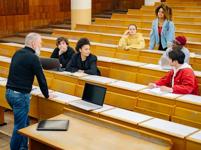 Students listening to a professor in a university lecture hall with laptops open