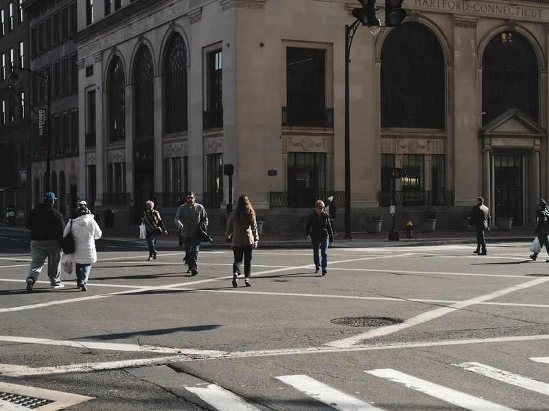 Pedestrians crossing a downtown Hartford street in front of historic stone buildings
