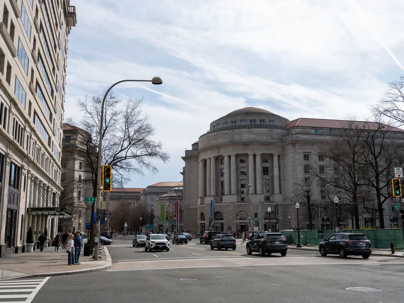 Pedestrians and traffic on a busy downtown street lined with historic stone buildings in Washington, DC