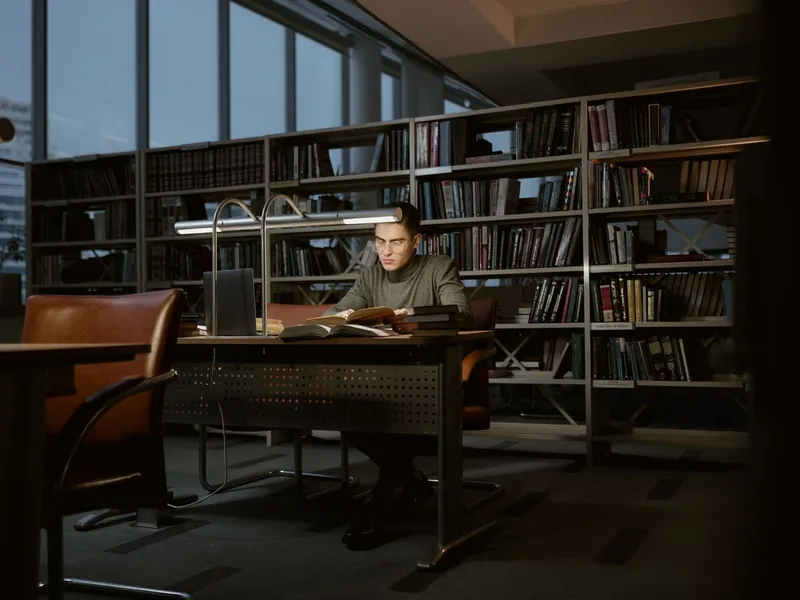 Researcher reading at a desk in a quiet library lined with bookshelves