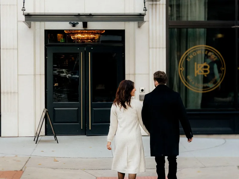 Couple walking hand in hand along a downtown sidewalk toward a restaurant entrance in Covington, Kentucky