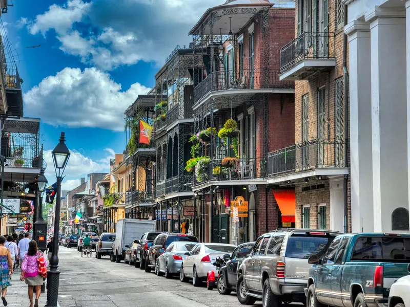 Pedestrians walk a French Quarter street in New Orleans lined with wrought-iron balconies and parked cars