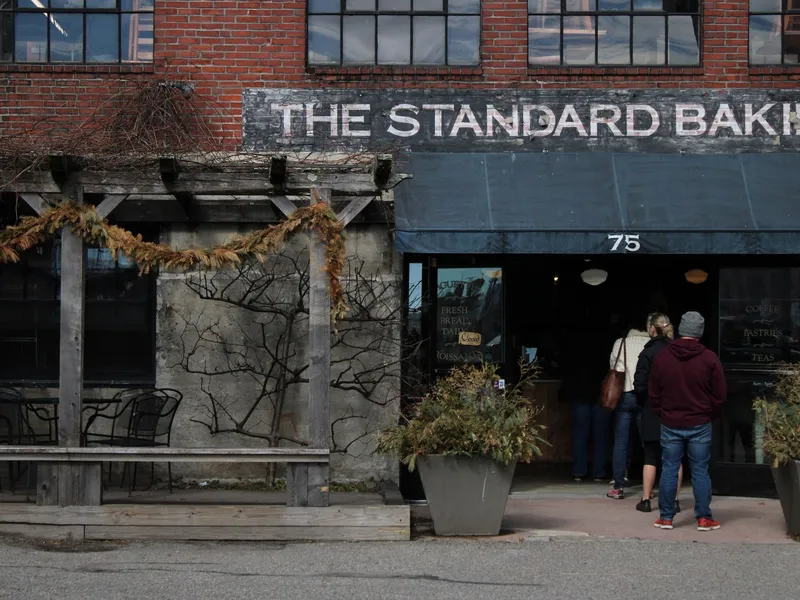 Customers lining up outside a brick bakery storefront with outdoor seating in Portland, Maine