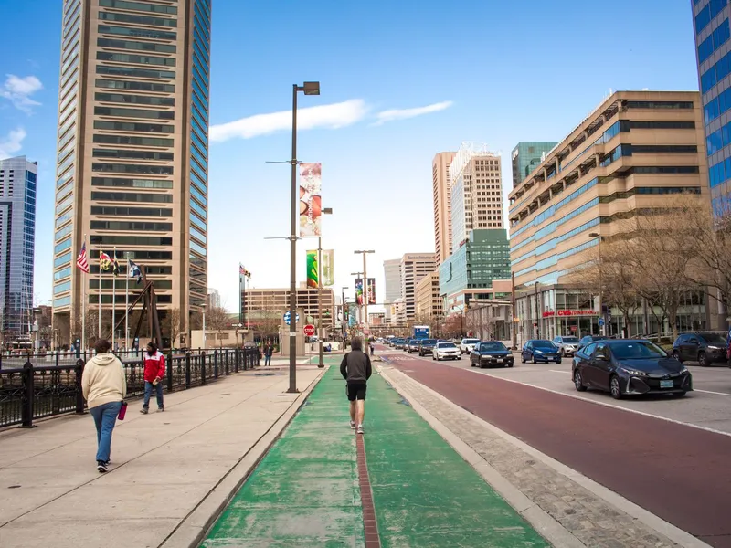 Pedestrians walking along a downtown Baltimore street lined with office towers and a bike lane