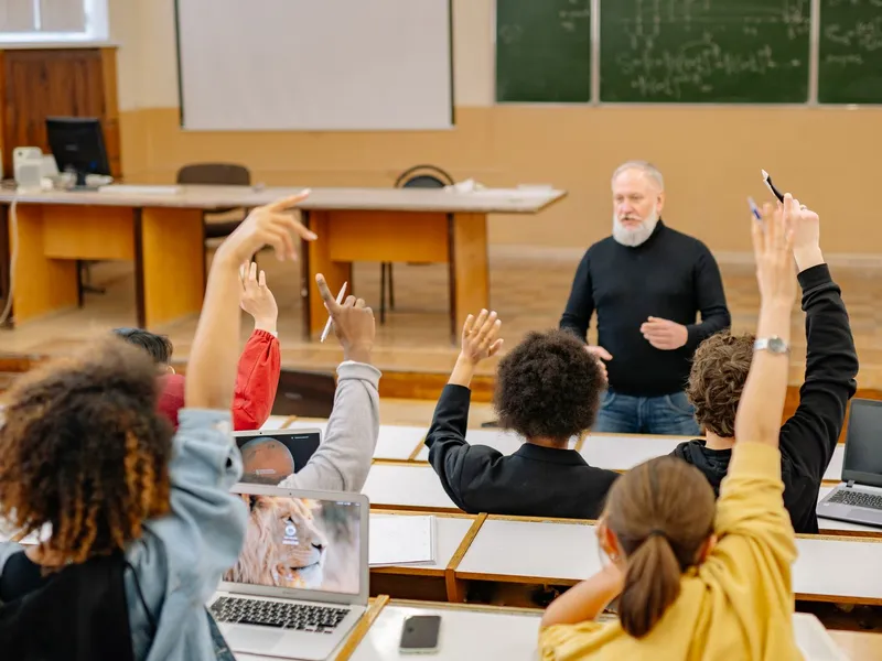 Students raising their hands to join a discussion led by a professor in a classroom