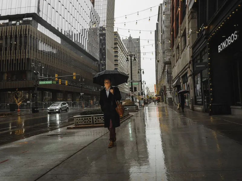 Pedestrian with an umbrella walking along a rainy downtown Detroit street lined with buildings