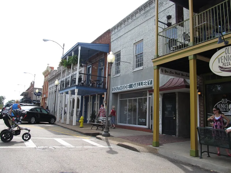 Shoppers and pedestrians on a sunny downtown street with balconied storefronts and a gallery in Oxford, Mississippi