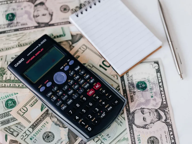 Calculator and notepad resting on a stack of US dollar bills for budget planning