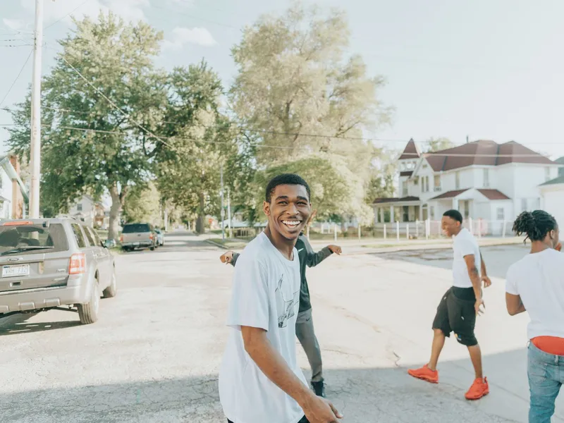 Young friends laughing together on a sunny residential street lined with trees and houses in Omaha