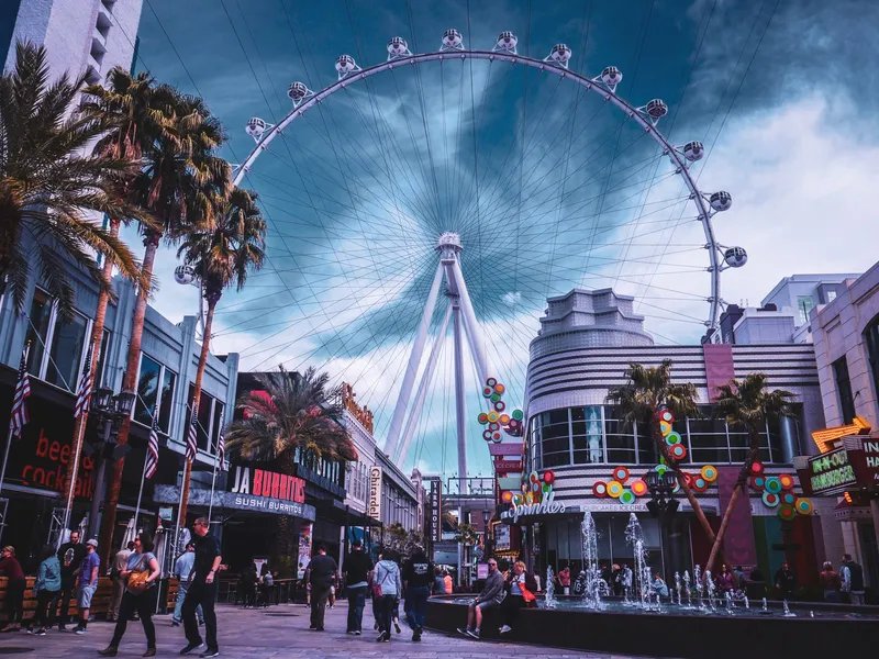 People strolling past shops, palm trees and a giant Ferris wheel in Las Vegas