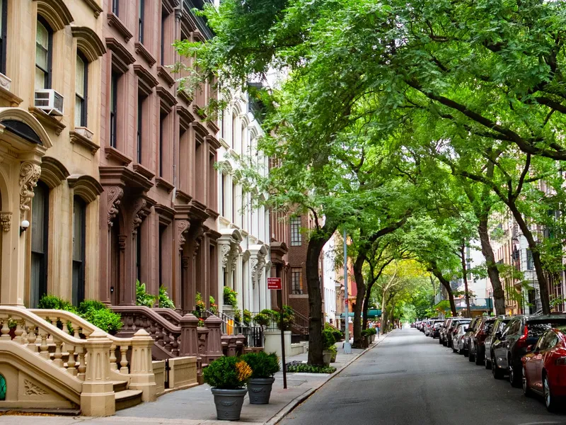 Tree-lined Brooklyn street with brownstone row houses, stoops and parked cars on a summer day
