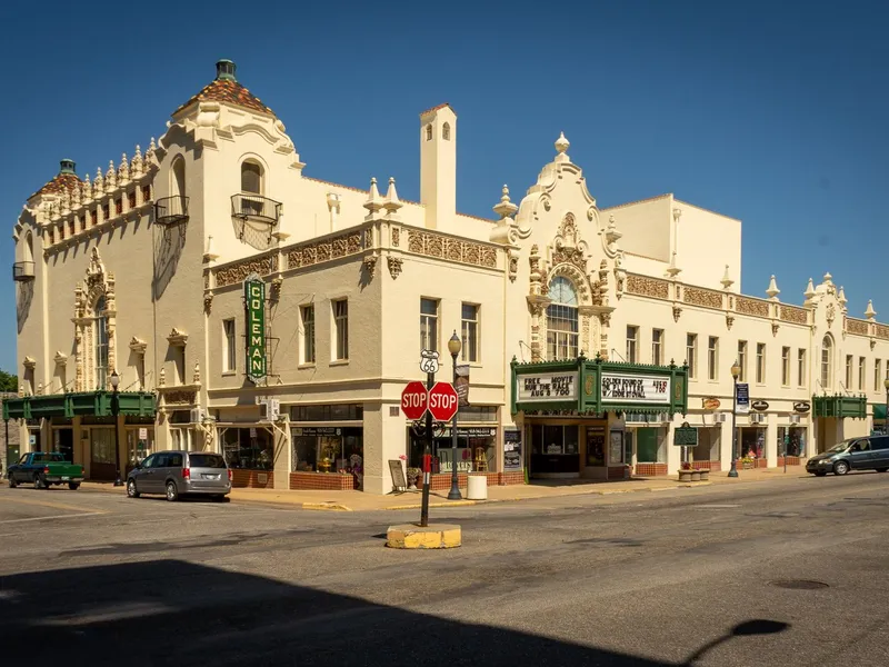 Small-town Oklahoma main street corner on Route 66 with an ornate historic theater, shops and parked cars